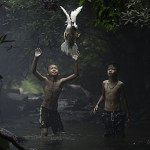 Hai cậu bé đang cố bắt con vịt gần một thác nước - © Sarah Wouters